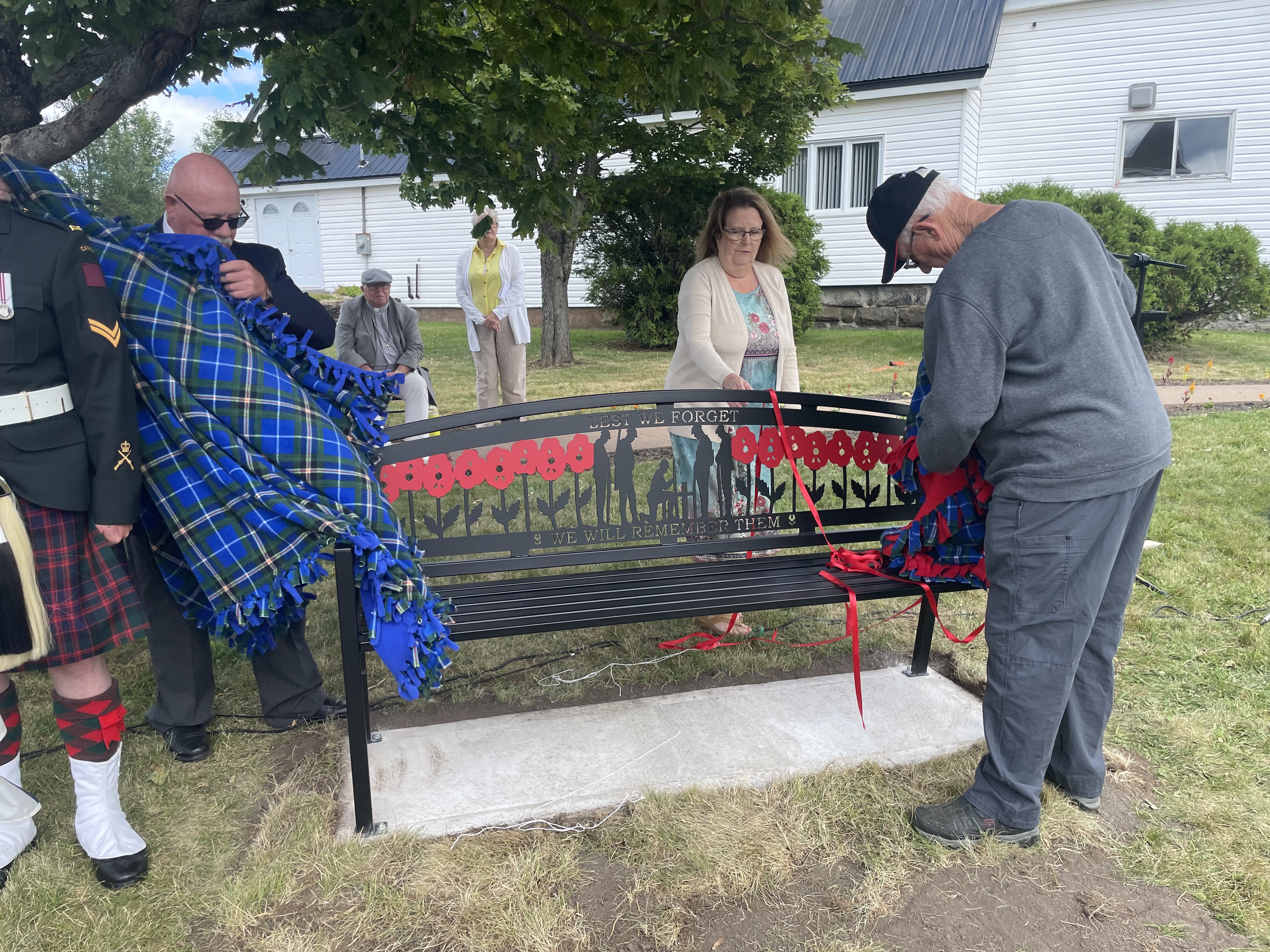 A man takes a blanket off a black metal bench while another man looks on. 